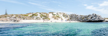 Summer time on a small island off Perth, Western Australia.  A photograph taken from the water looking back to the beach where people are swimming, sunbathing and walking on the limestone cliffs.