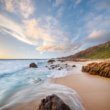 A beautiful, pristine beach in the Margaret River region of Western Australia.  The water washing in around granite rocks while the sun sets with a warm orange glow on the granite cliffs above the beach.   Photograph by renowned photographer, Christian Fletcher.
